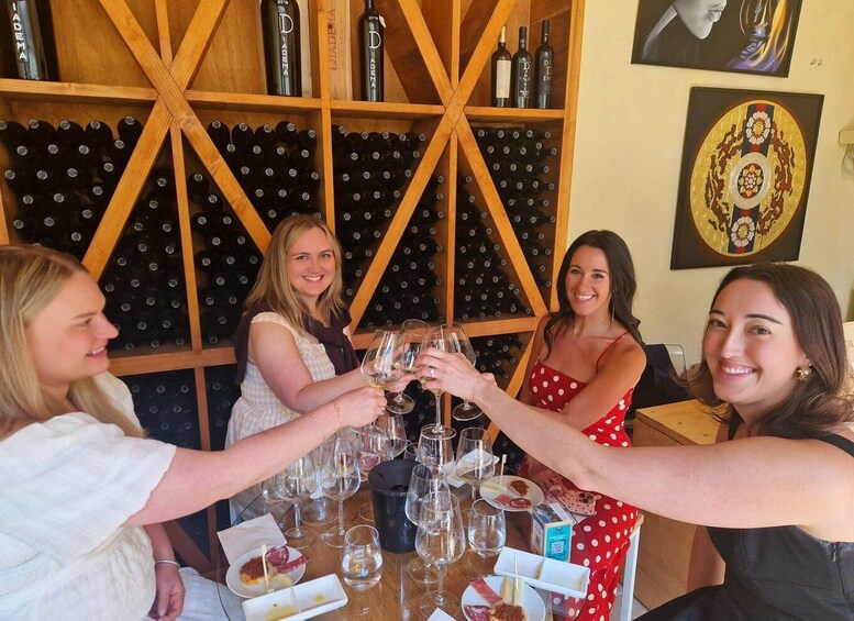 A group of people toasting with wine glasses at a table with a wine rack in the background. 1