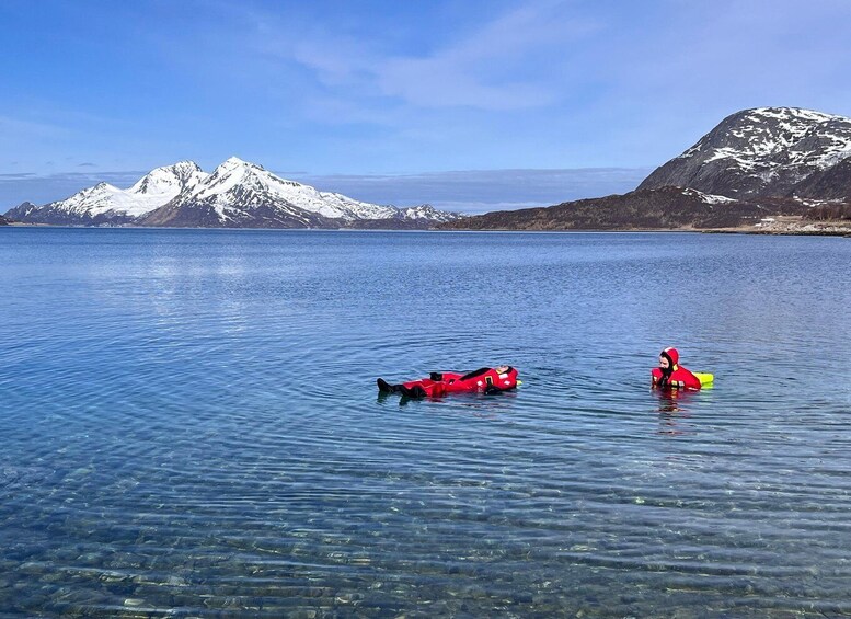 Two people in red life jackets floating on a calm lake with snow-capped mountains in the background. 5
