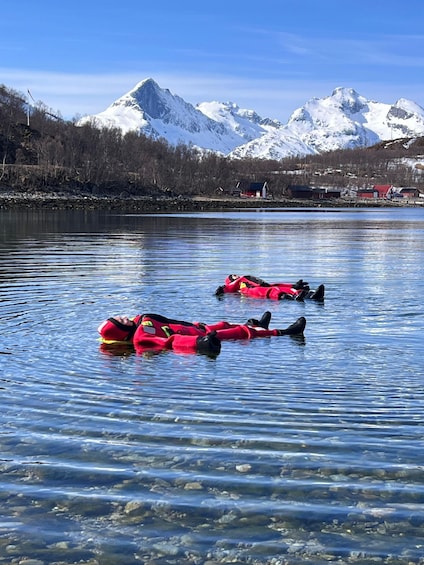 Two people in red life jackets floating on a calm lake with snow-capped mountains in the background. 1