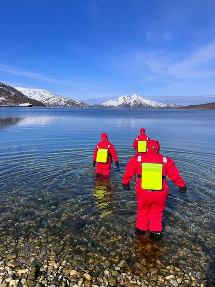 Three people in red suits wading in a clear lake with snow-capped mountains in the background. 4