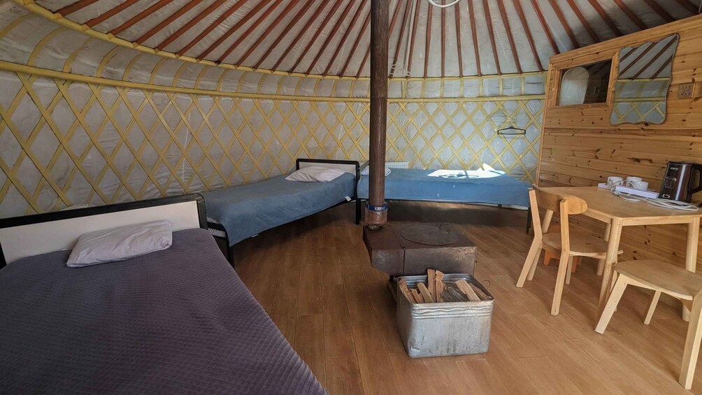 A yurt interior with two beds, a table, and a stove. 5