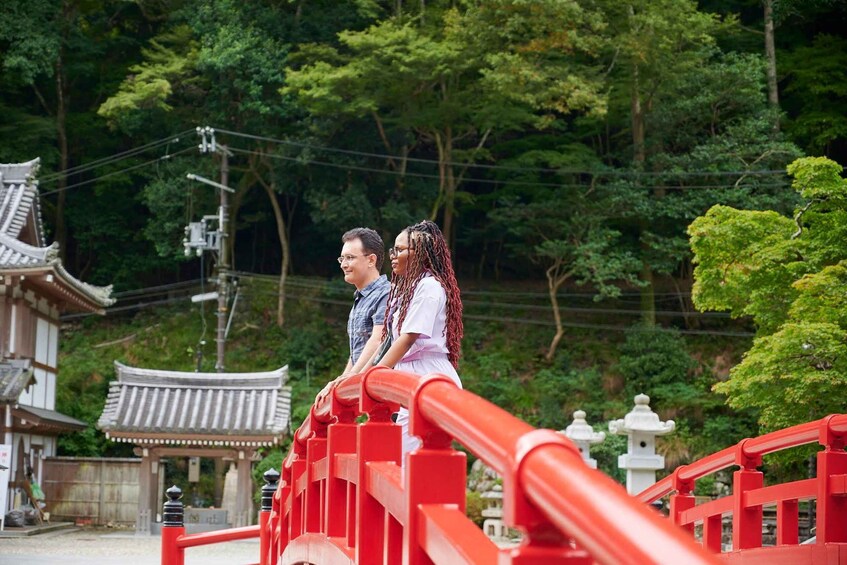 A couple on a red bridge with traditional Japanese architecture in the background. 1