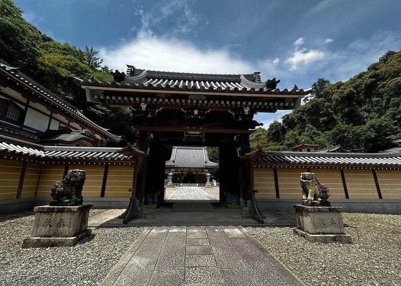A traditional Japanese gate with stone lion statues, surrounded by a gravel courtyard and traditional buildings. 3