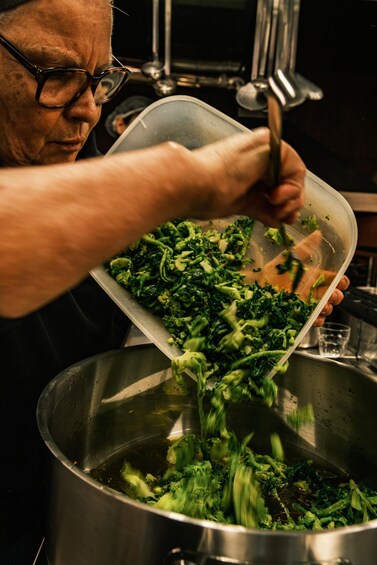 A person pouring chopped broccoli into a pot. 1