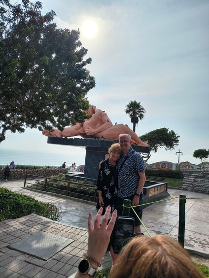 A couple posing in front of a sculpture with a palm tree and a body of water in the background. 4
