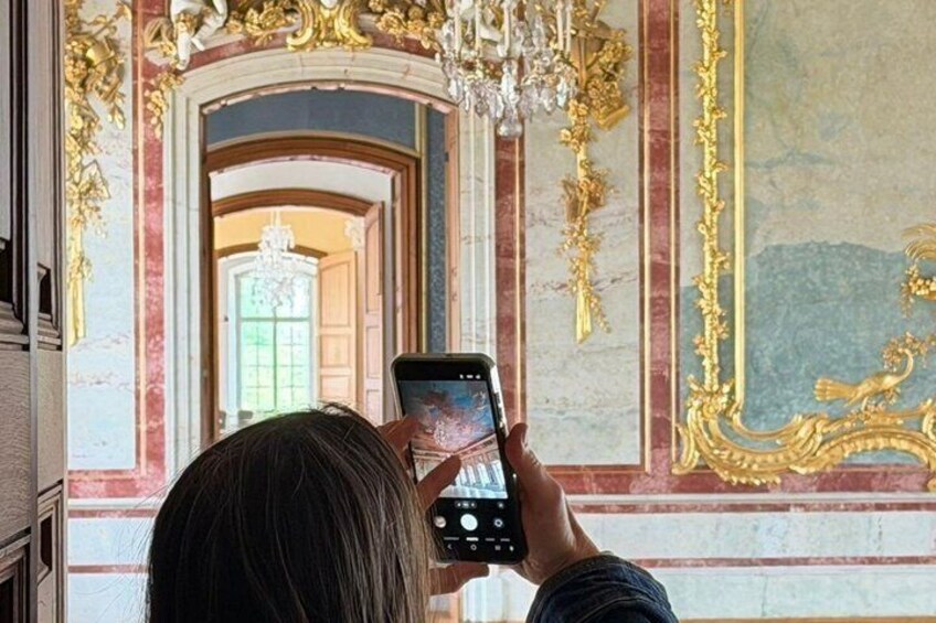A person taking a photo with a smartphone in a room with ornate gold decorations and a mirror. 5