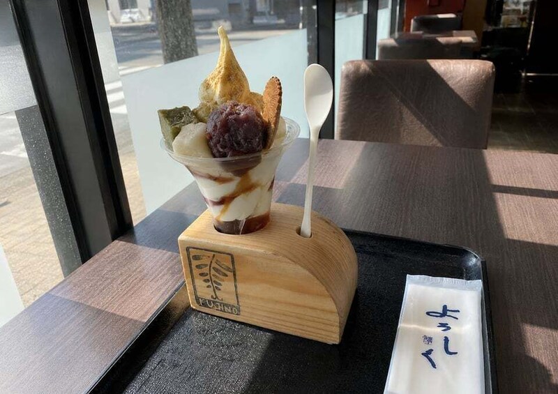 A dessert on a wooden stand with a spoon, a menu, and a window view. 2