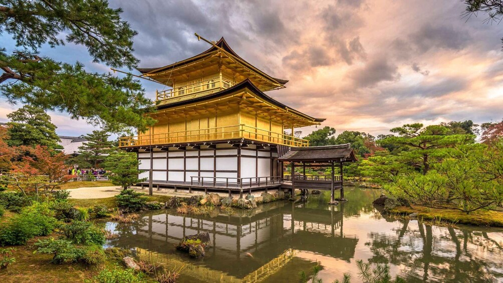 A traditional Japanese pagoda with a reflection in a pond, surrounded by trees and a cloudy sky. 1