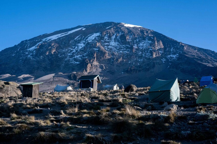 A mountain with a snow-capped peak, several tents, and a small wooden structure. 2