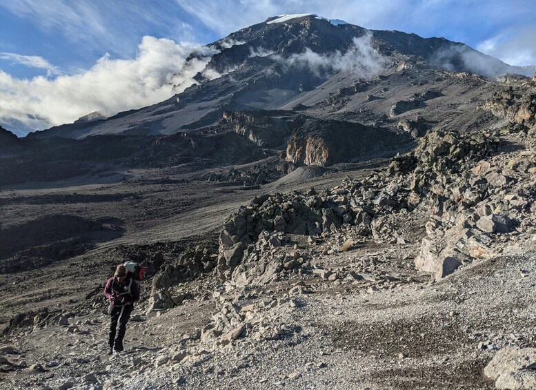 A hiker on a rocky mountain trail with a snow-capped peak in the background. 1