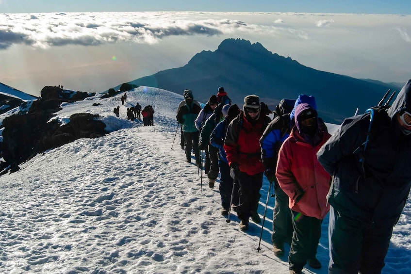A group of hikers on a snowy mountain trail with a mountain in the background. 3