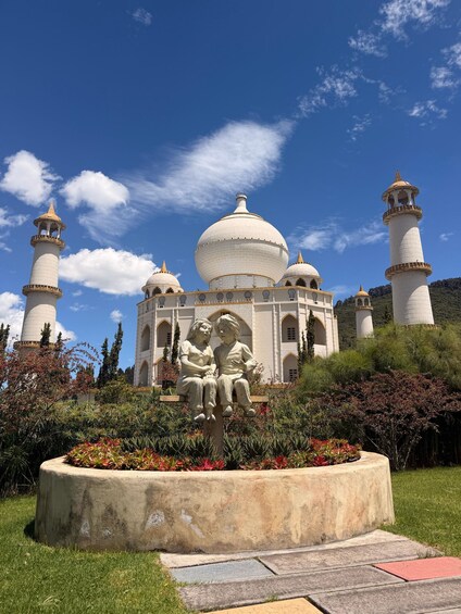 A white building with domes and minarets, surrounded by greenery and a stone bench with a sculpture. 2