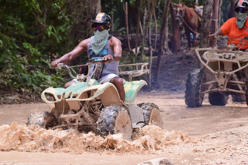 Two people riding atv's through a muddy area. 3