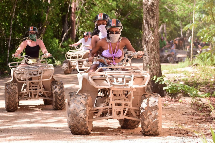 People riding ATVs on a dirt path surrounded by trees. 1