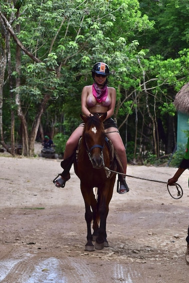 A woman riding a horse on a dirt path surrounded by trees. 2