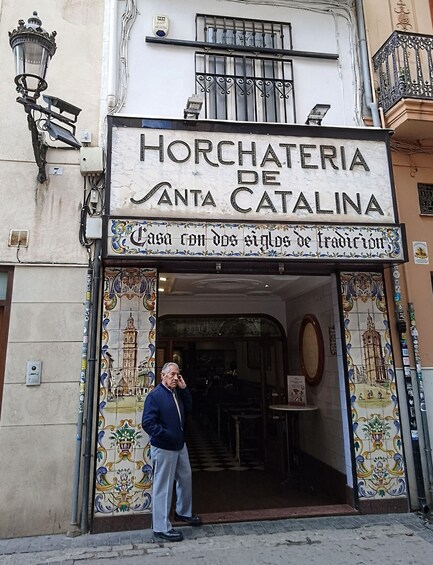 A man standing in front of the entrance to Horchateria de Santa Catalina, a traditional Catalan house. 4