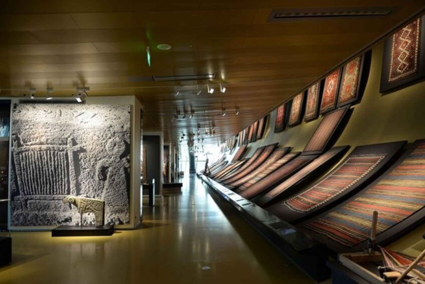 A museum corridor with a stone wall and a display of woven textiles. 5