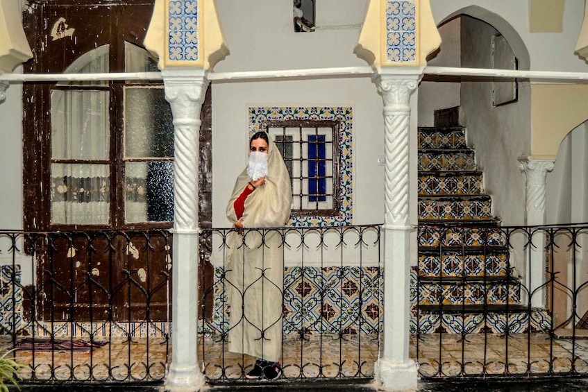 A person standing on a balcony with a patterned floor, a decorative railing, and a staircase with colorful tiles. 1