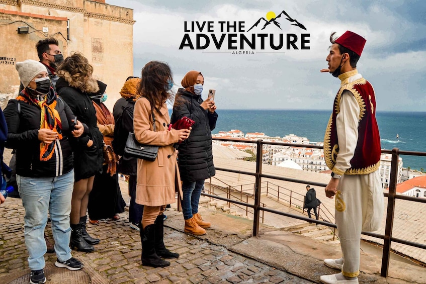 A group of people on a coastal promenade, a person in traditional attire, and the text "LIVE THE ADVENTURE ALGERIA". 3