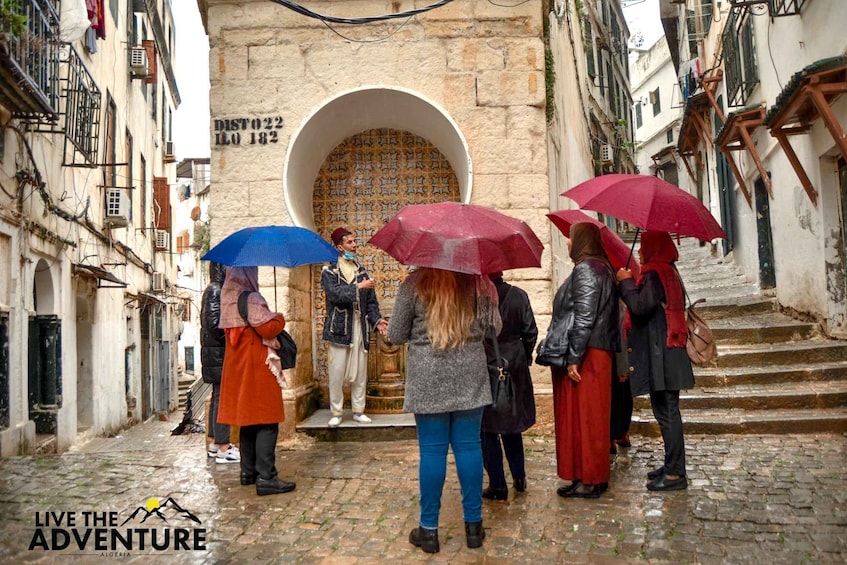 A group of people walking down a cobblestone street with umbrellas, approaching a building with a large arched doorway. 2