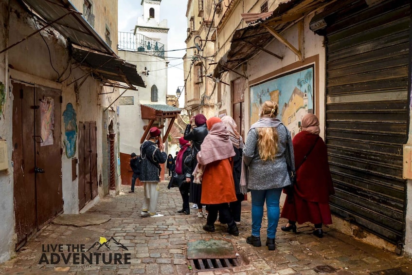 A narrow cobblestone street lined with buildings, some with closed shutters, and a few people walking. 4