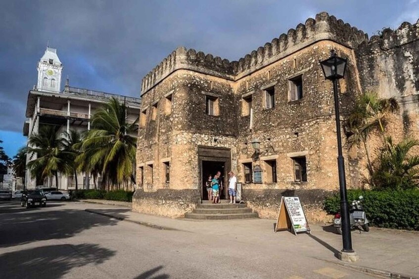 Vecchio edificio in pietra con una torre dell'orologio, palme e un cartello. 2