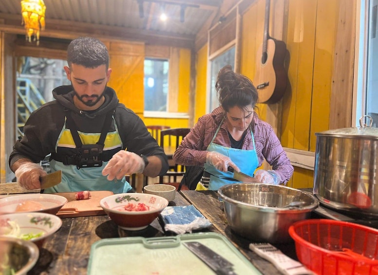 Deux personnes préparent un repas dans une cuisine aux murs en bois, avec une guitare en arrière-plan. 1