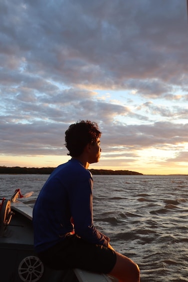 A person sitting on a boat, looking out at the water during sunset. 4