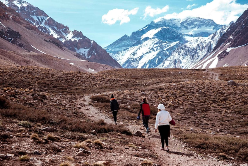 A mountainous landscape with a dirt path, snow-capped peaks, and sparse vegetation. 2