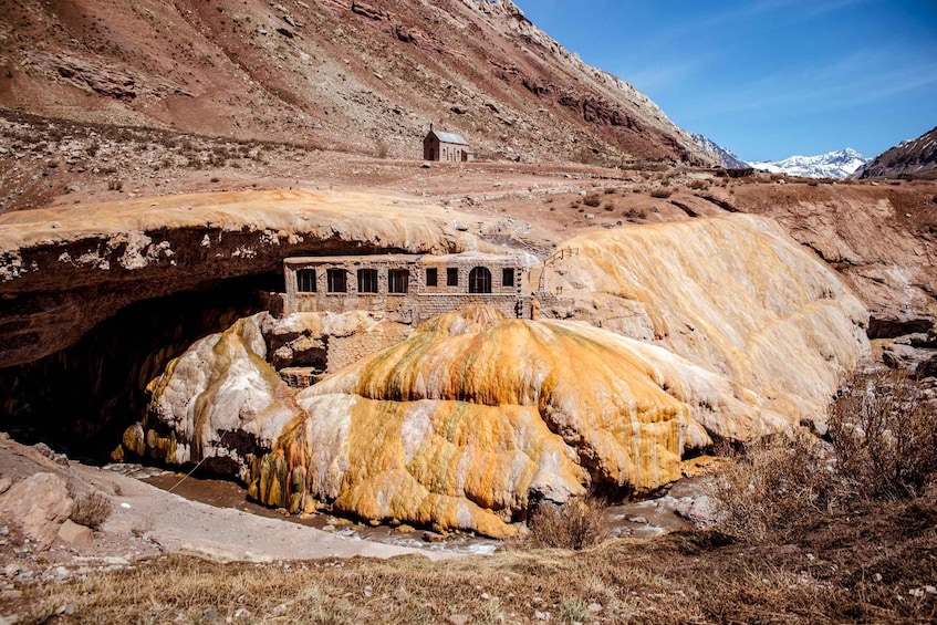 A cave with a small building inside, surrounded by yellow and white rock formations. 5