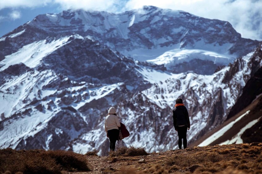 Two people standing on a mountain ridge with snow-covered peaks in the background. 4
