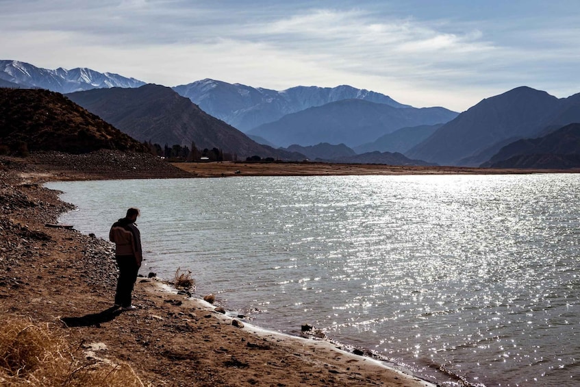 A person standing by a lake with mountains in the background. 1