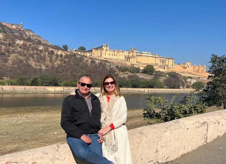 A couple standing by a river with a historic fort in the background. 1