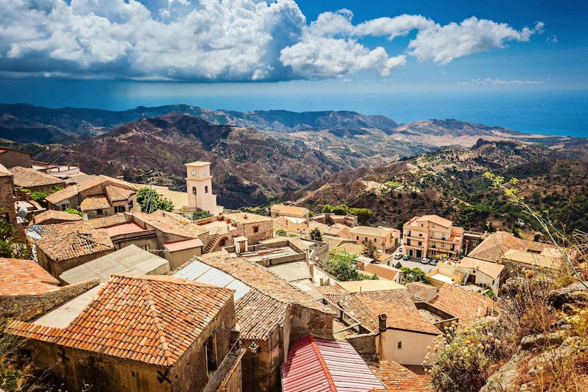 A coastal village with terracotta-roofed buildings, a prominent tower, and a mountainous backdrop. 3