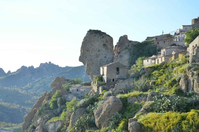 A rugged landscape with a prominent rock formation, a small building, and a cluster of houses on a hillside. 5