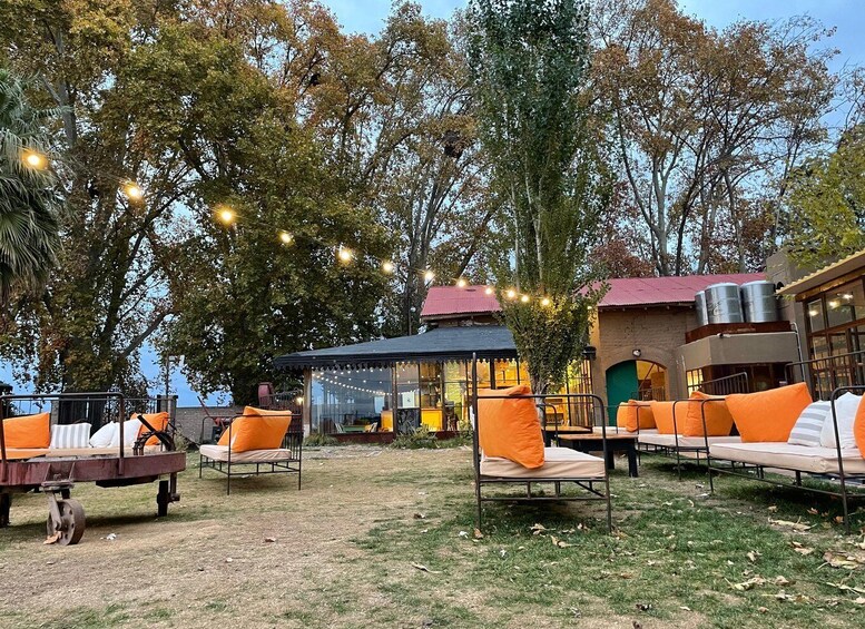 An outdoor seating area with orange cushions and a metal table, surrounded by trees and a building with a red roof. 3