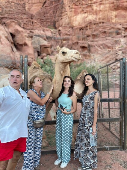 A group of people with a camel in a rocky enclosure. 1