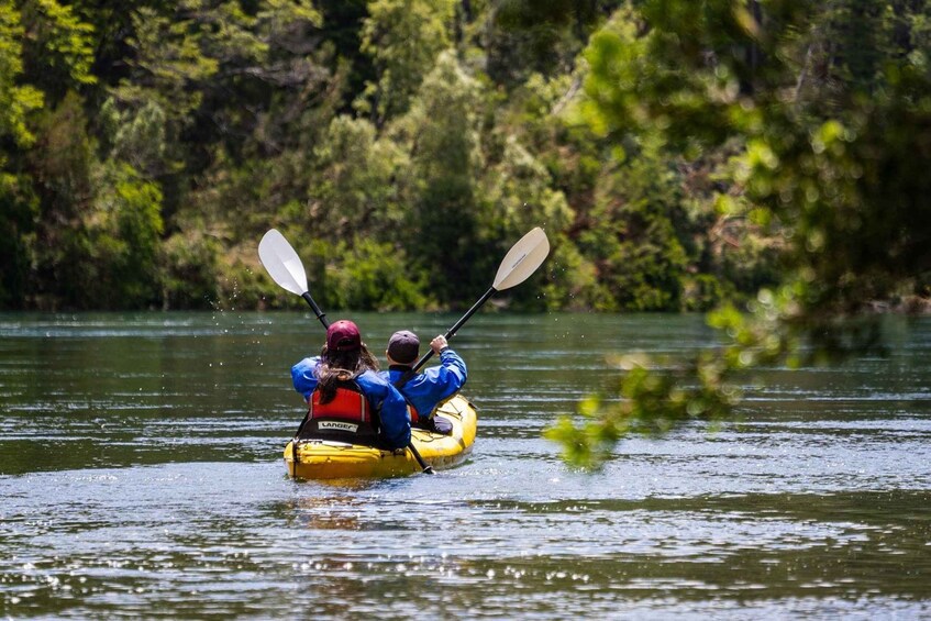 Two people kayaking on a river surrounded by dense forest. 5