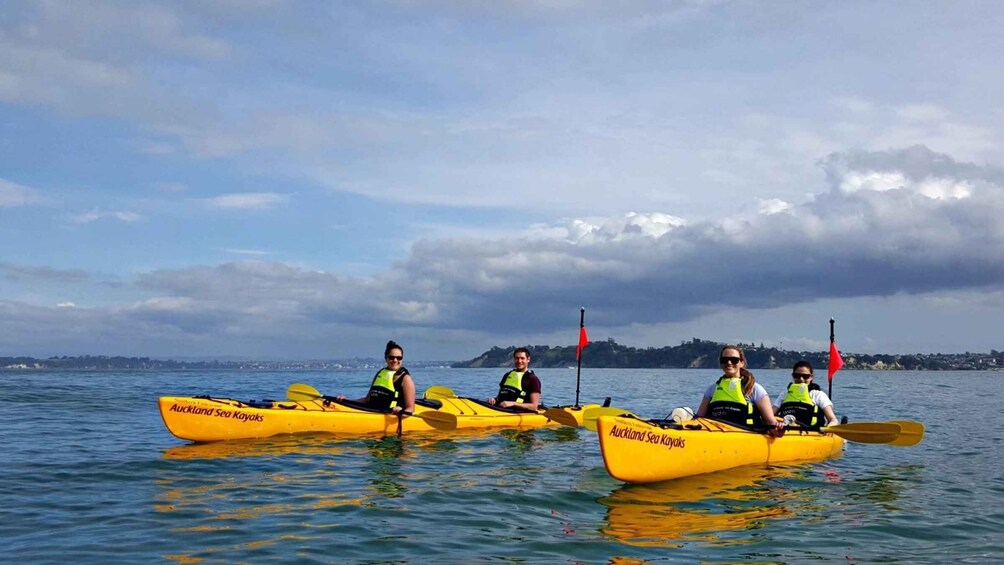 Three people in yellow kayaks on a calm body of water with a cloudy sky and distant land in the background. 1