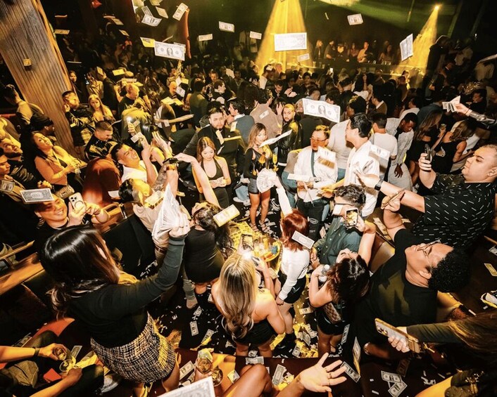 A crowded indoor event with people holding dollar bills. 3