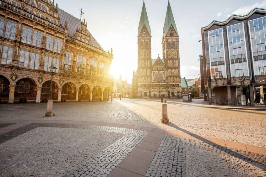 A cobblestone square with historic buildings, including a church with twin spires. 2