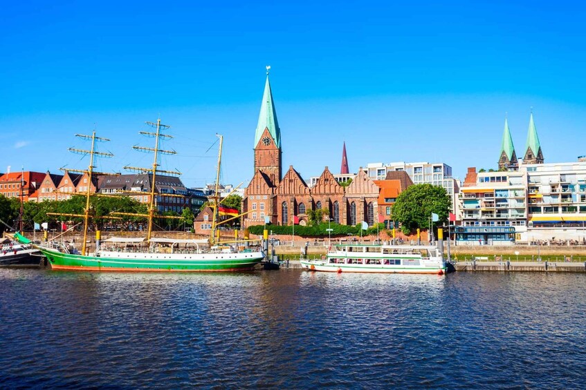 A green and white sailing ship docked at a harbor with a tall church spire in the background. 5