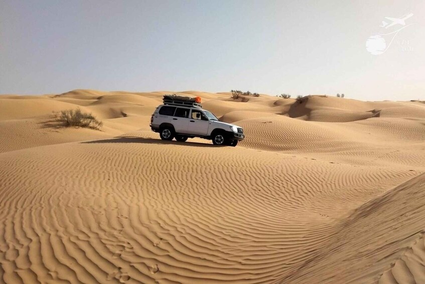 A white SUV on a sandy dune with rippled sand patterns. 1