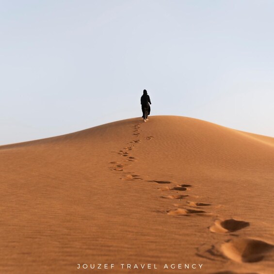 A person walking on a sand dune with footprints. 4