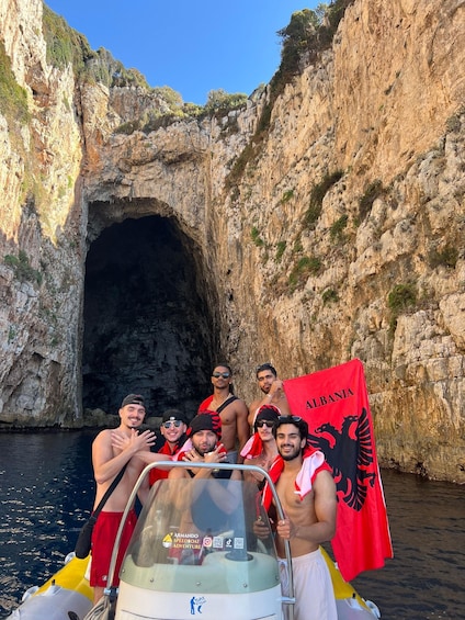 A group of people on a boat near a rocky cave entrance, with a flag reading "Albania". 1
