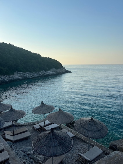 A beach with lounge chairs and thatched umbrellas overlooking turquoise waters and a rocky coastline. 4