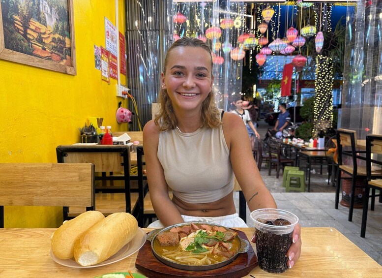 A person sitting at a table with a plate of food, a drink, and bread. 1