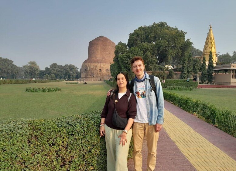 A couple standing in a park with a large dome-shaped building and a golden spire in the background. 2