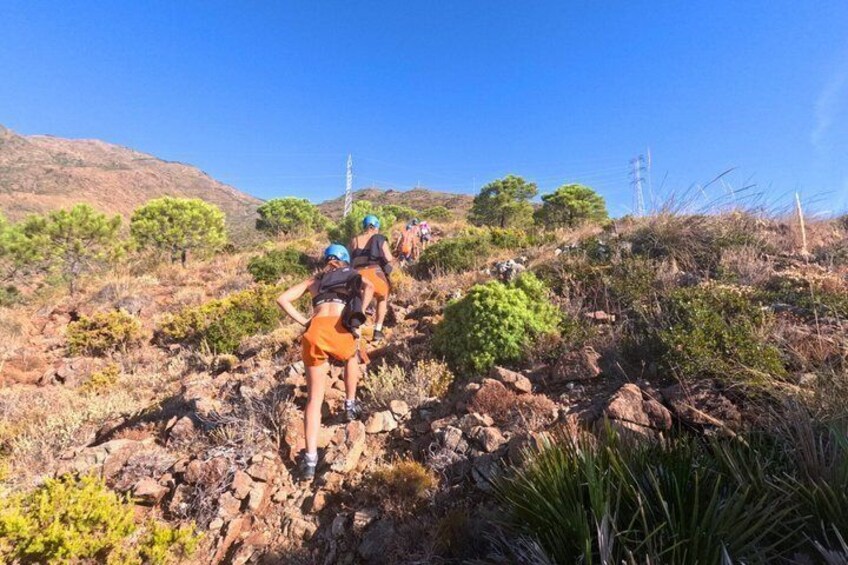 A group of hikers ascending a rocky hillside with sparse vegetation and a clear blue sky. 2