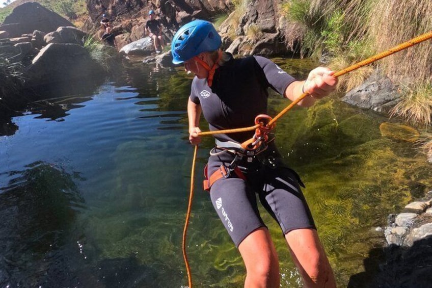 A person rappelling into a clear water body surrounded by rocks. 4